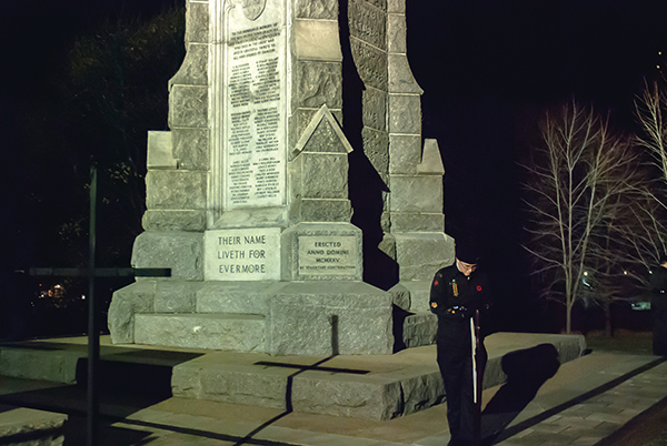 Military member standing in front of a vigil with his head down by a statue