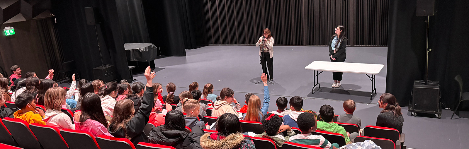 Person in a theatre speaking to kids, all sitting in read theatre seats