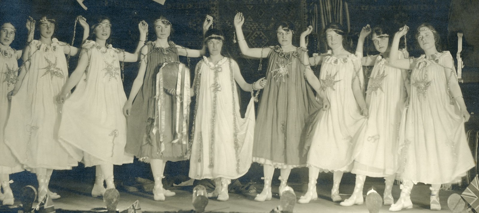 Black and white photo of nine women standing on stage in various poses, 1918