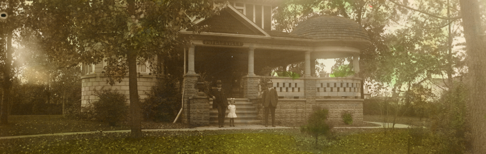 Faded photograph of a large house with two men and a little girl standing in front. 