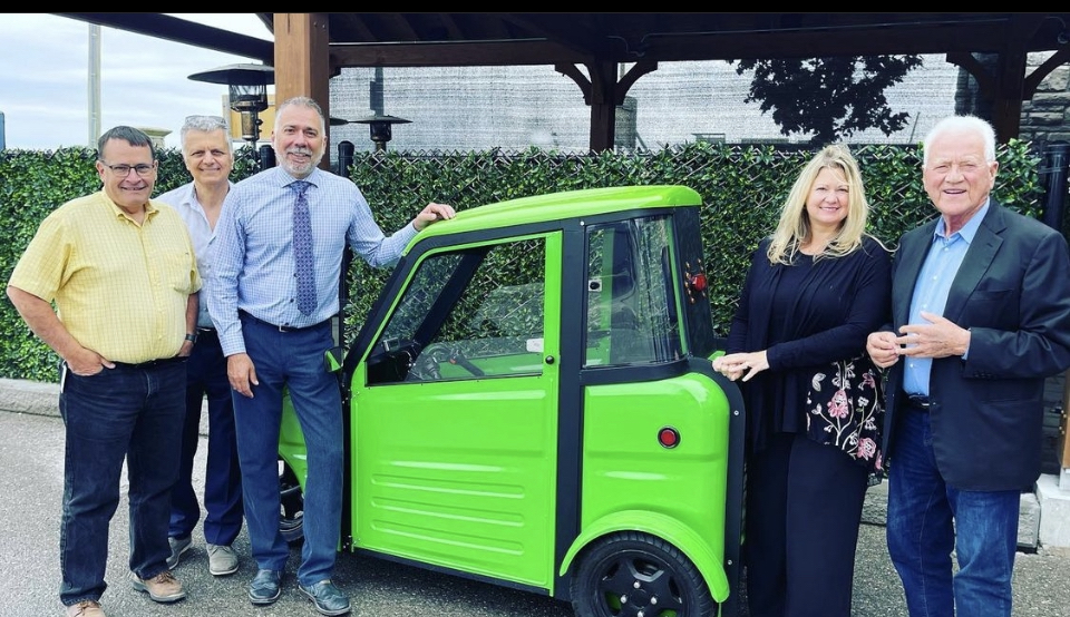 Mayor and Town staff standing next to electric vehicle with Frank Stronach