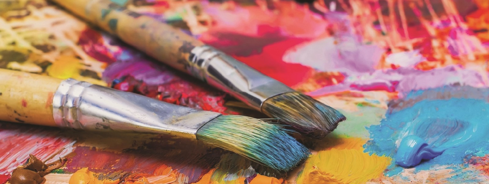 Two dirty paint brushes on a surface full of coulourful paint smudges