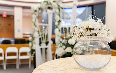Bowl of flowers with wedding arch behind, inside Council Chambers