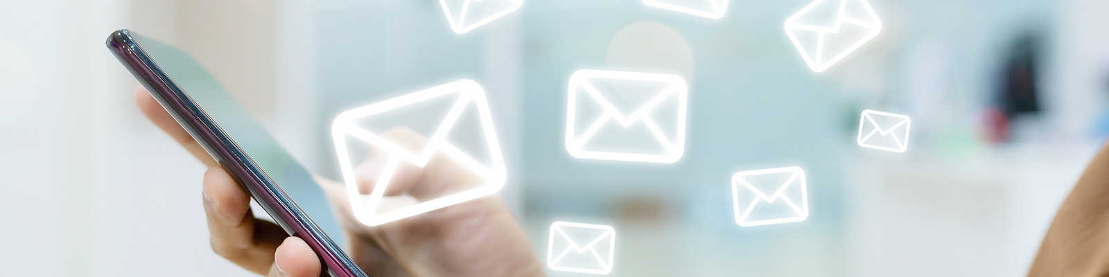 Hand holding a cellphone with email icons floating around it.