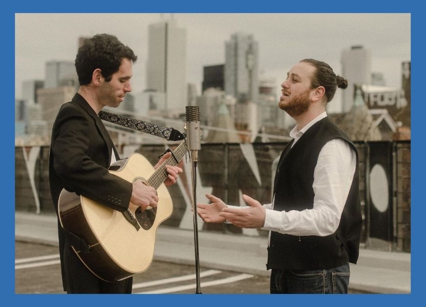 Two men facing each other singing and playing the guitar
