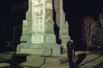 Military member standing in front of a vigil with his head down by a statue