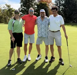 Four men on a golf course, two holding golf clubs