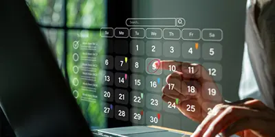 Person sitting at a laptop and choosing a date on a see-through virtual calendar in the air
