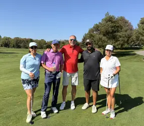 Three men and two women on a golf course, four holding golf clubs
