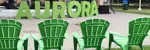 Four green lawn chairs on grass facing AURORA green letters on band stage