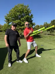 Two men standing on green grass, one holding a green tube