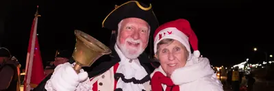 Town Crier and lady wearing red hat at Santa parade event
