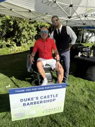 Two men under a tent, one sitting on a barber's chair