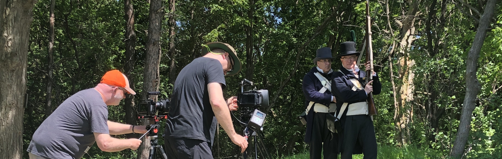 Fil crew recording two men in old outfits, with an old rifle, in a forest