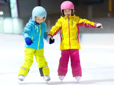 Two young kids ice skating indoors rink