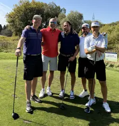 Five men on a golf course, four holding golf clubs