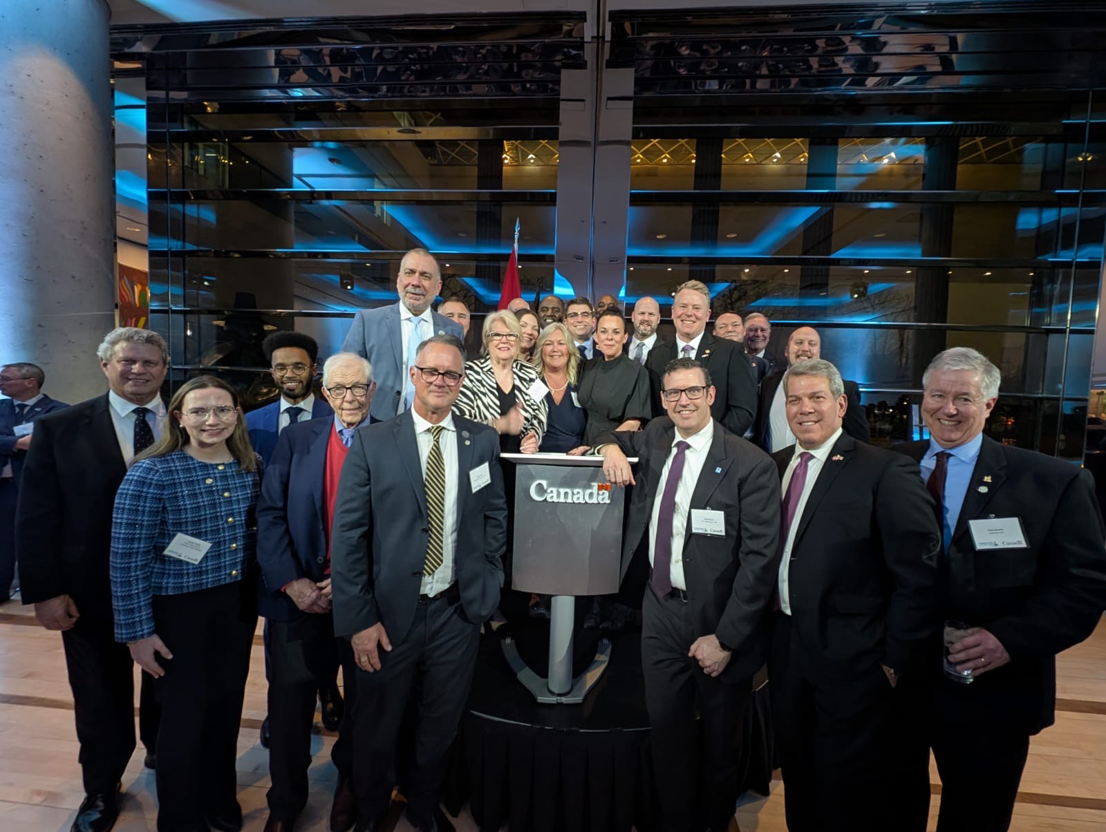 Mayor with a group of people posing for a picture, around a podium with the word Canada on it