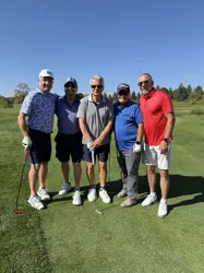 Five men on a golf course, four holding golf clubs