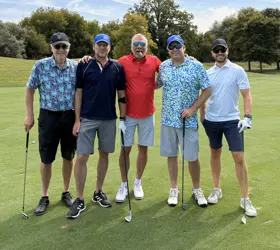 Five men on a golf course, four holding golf clubs