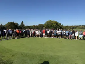 A very large group of people, standing side by side on a golf course, posing for a picture