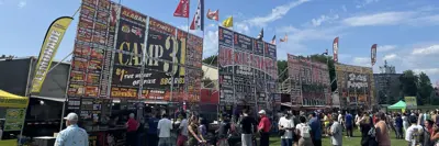 Wide view of four ribfest food signs and group of people at event in park