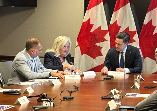Three people at a board room table with Canada flags in the background