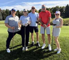Three men and two women on a golf course, four holding golf clubs