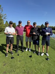 Five men on a golf course, four holding golf clubs