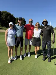 Two woman and two men on a golf course, four holding golf clubs