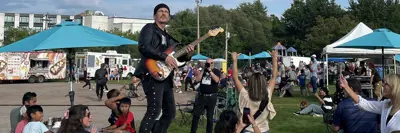 Musician holding guitar standing on top of wooden picnic table concert in park