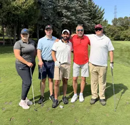 Five men on a golf course, four holding golf clubs