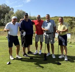 Five men on a golf course, four holding golf clubs