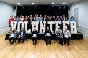 Award winners on and in front of a stage with a very large lit Volunteer sign